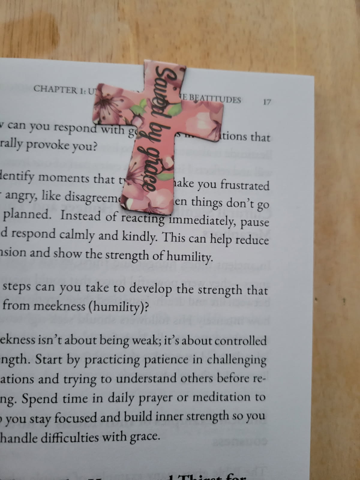 Cross-shaped magnetic bookmark with pink floral design clipped inside an open book, featuring an encouraging Christian phrase.