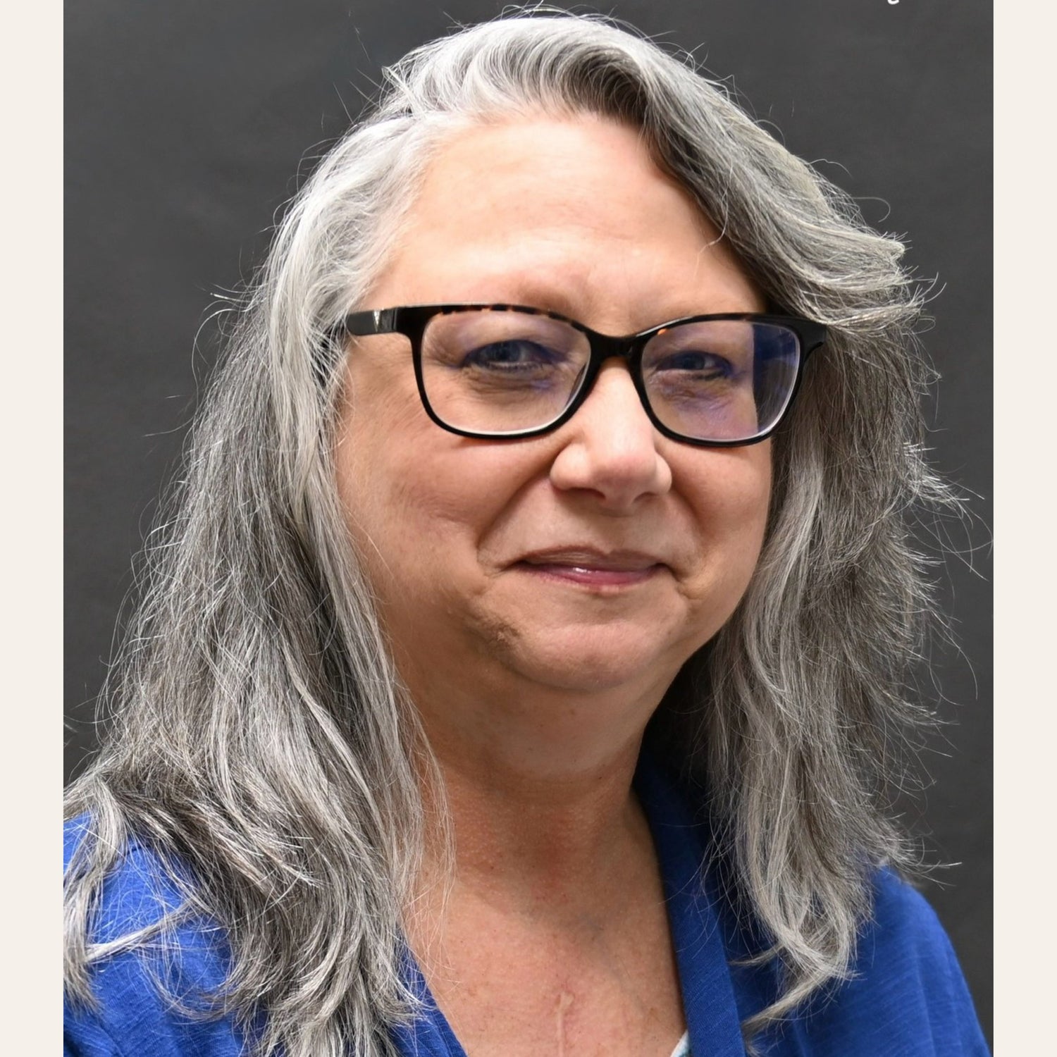 Professional portrait of Christian author L. M. Duvall with long gray hair, glasses, and a blue blouse.