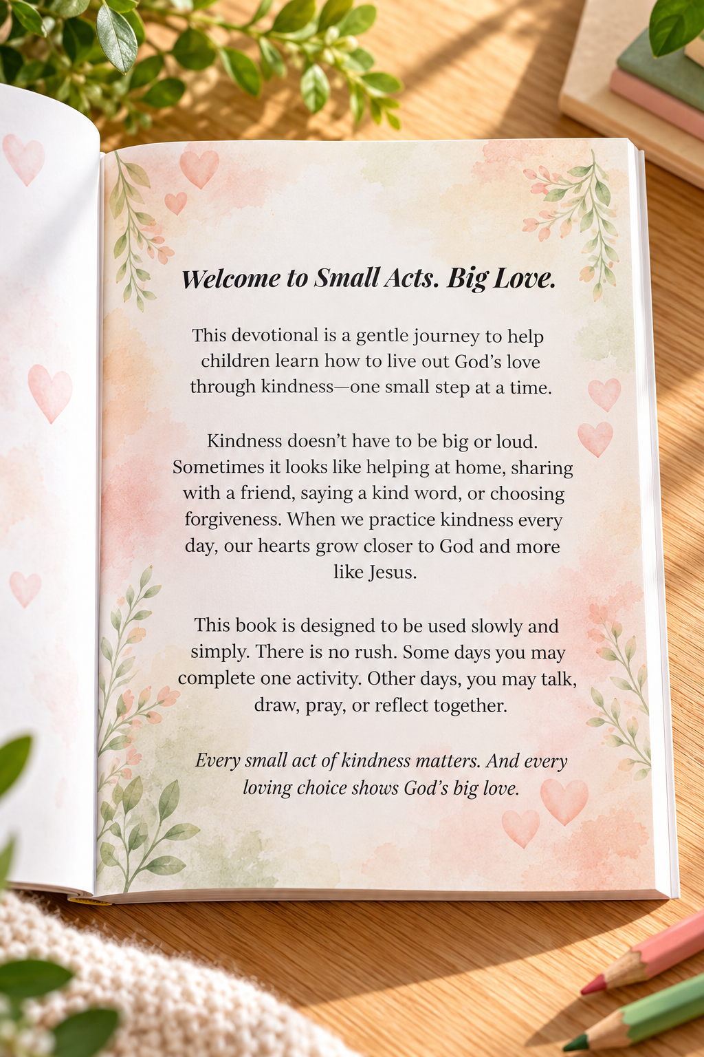 Open paperback of Small Acts. Big Love., a 4-week children’s Christian devotional by L. M. Duvall, displaying the original Welcome page with watercolor flowers, hearts, and a message about kindness and God’s love, on a light oak tabletop with greenery and colored pencils